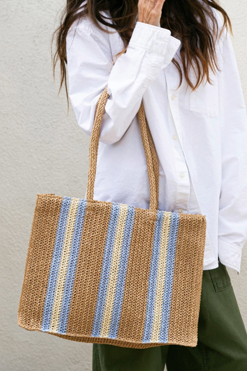 Person holding a striped woven Wyeth bag against a plain background